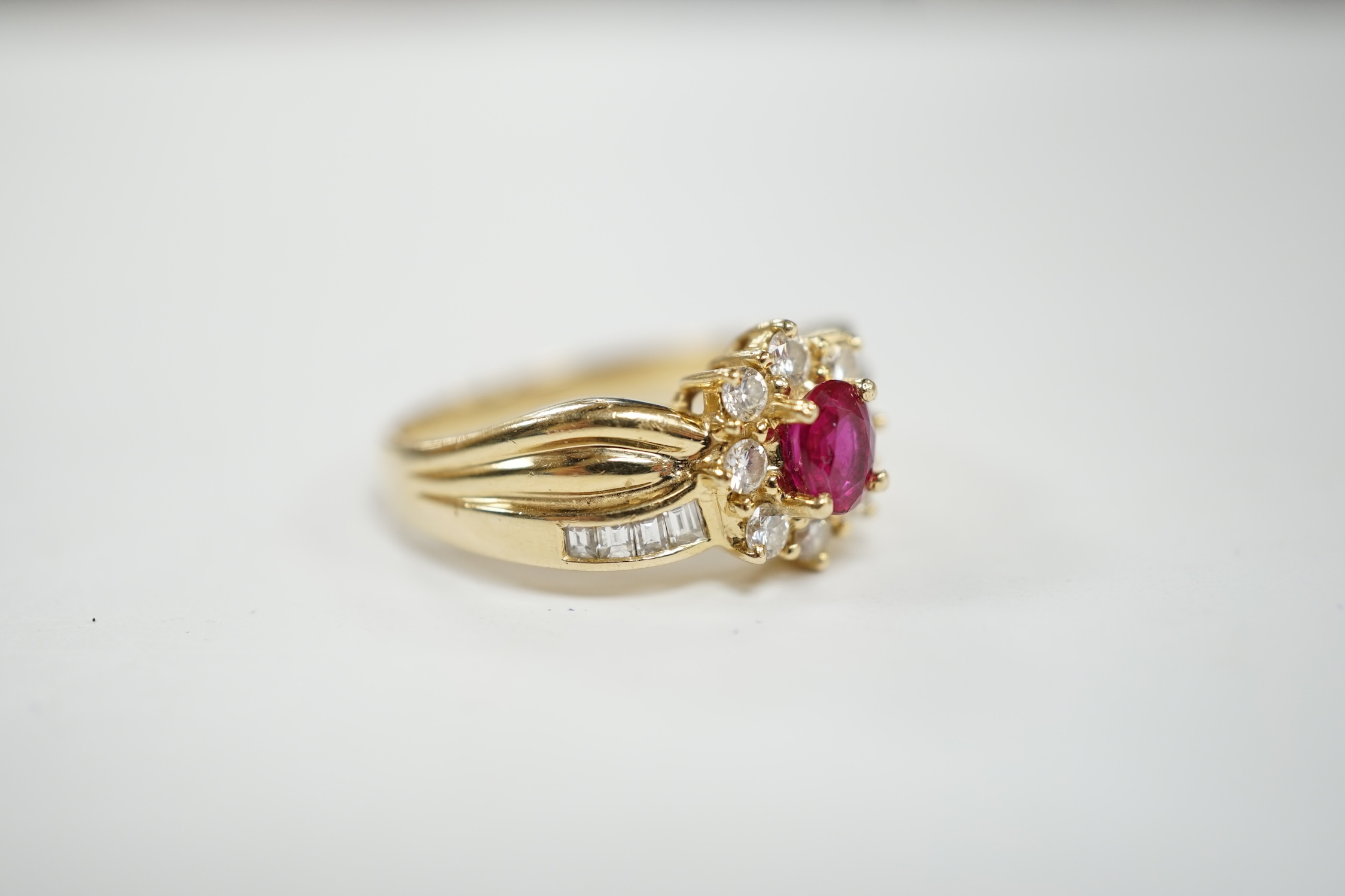 A modern 14k, ruby and diamond set oval cluster dress ring, with diamond chip set shoulders, size P, gross weight 5.1 grams.